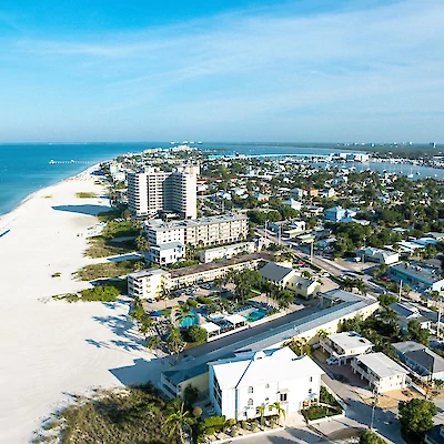 Aerial view of a coastal city with sandy beaches, high-rise buildings, residential houses, and a clear blue sky ending the sentence.